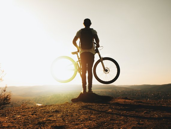 Biker läuft mit seinem Rad in der Hand in das Sonnenlicht