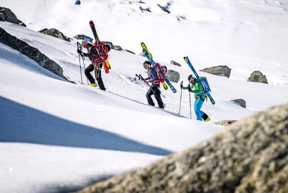 Drei Skitourengeher tragen ihre Ski am Rucksack