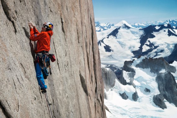 David Lama beim Klettern mit verschneitem Bergpanorama im Hintergrund.