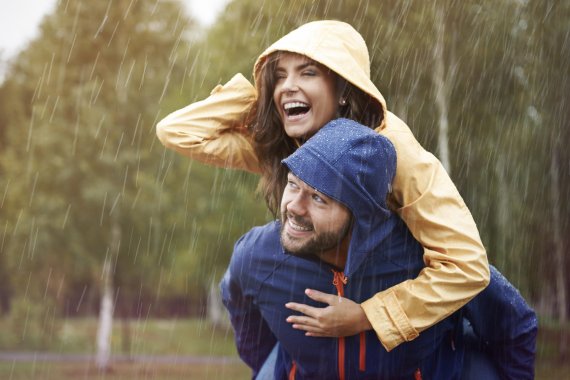 mb-Regenschutz-Funktionskleidung Frau in gelber Jacke hüpft im Regen auf blauen Mann