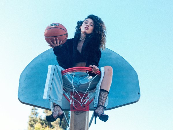 Woman sitting in the basketball hoop and holding a basketball