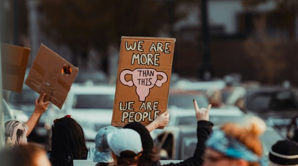 Frauen protestieren. Schild im Fokus zeigt "We are more than this - we are people"